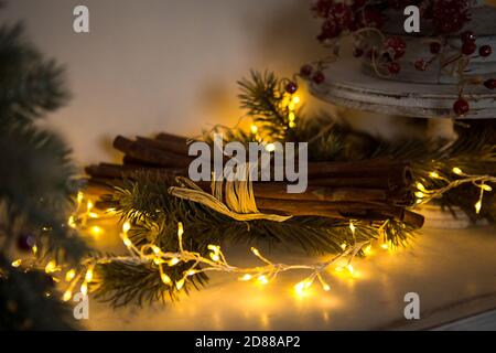 Bâtons de cannelle noués avec une ficelle dans des guirlandes de lumières jaunes sur des branches d'arbre de Noël et des baies rouges. L'atmosphère du nouveau groupe festif de l'année Banque D'Images