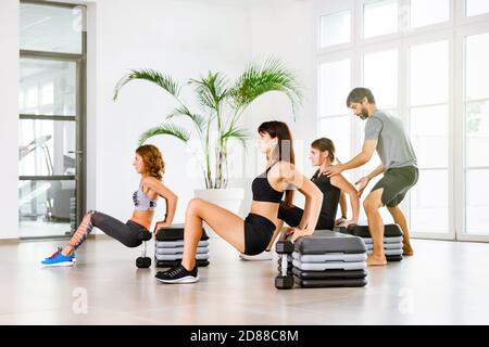 Cours de fitness avec des jeunes faisant de l'exercice poussé vers le bas avec un entraîneur personnel aidant dans une salle de gym de haute clé dans une santé et une forme physique ou une vie saine Banque D'Images