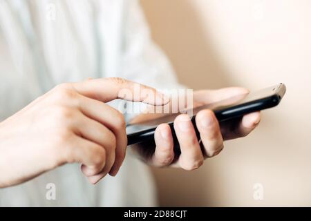 Les mains des femmes tiennent un téléphone noir, en appuyant sur un smartphone avec un doigt, en le touchant. Gros plan, mise au point douce Banque D'Images