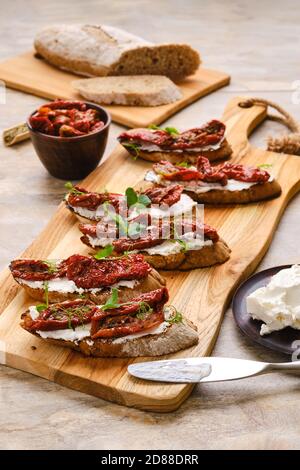 Toasts au fromage de chèvre et tomates séchées sur découpe de bois carte Banque D'Images