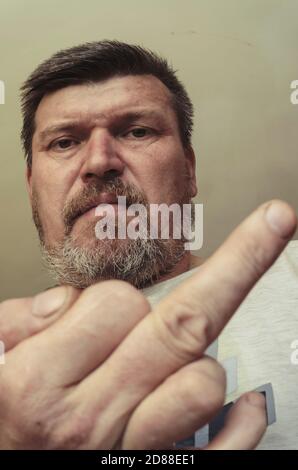 Portrait inhabituel d'un homme montrant un geste du milieu du doigt. Un homme adulte avec une barbe fait un geste décent et regarde l'appareil photo. Banque D'Images