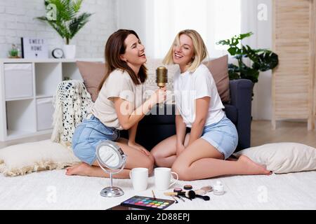 concept d'amitié et de fête à la maison - portrait de deux de belles filles s'amusent ensemble et chantent karaoké sur les cheveux brosse dans le salon confortable Banque D'Images