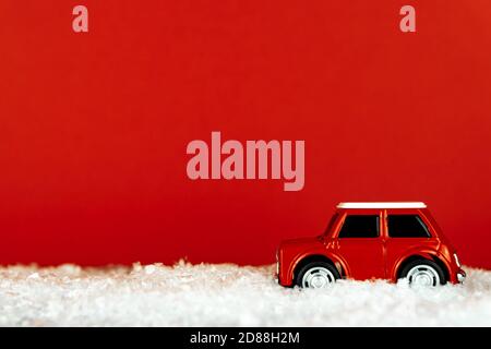 Une petite voiture de jouet rouge roule sur une route enneigée sur fond rouge. Carte de vœux de Noël avec espace pour les copies Banque D'Images