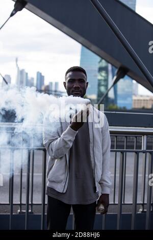 Vue avant du jeune homme noir tenant une bombe à fumée. Regarder l'appareil photo. Trois quarts de longueur. Verticale. Banque D'Images
