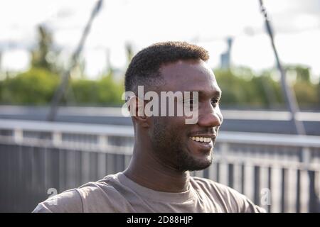 Jeune homme ethnique africain souriant à l'extérieur. Vue latérale. Portrait. Gros plan. Au-dessus des épaules. Banque D'Images