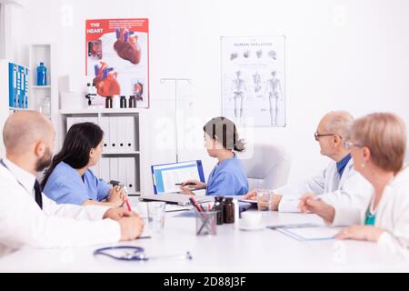 Une infirmière tient une planchette à pince expliquant son diagnostic devant des experts en médecine pendant le séminaire. Thérapeute en clinique parlant avec des collègues de la maladie, professionnel de la médecine Banque D'Images