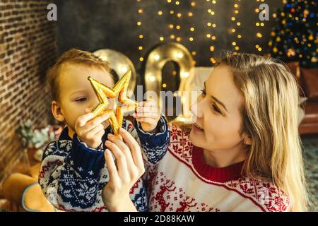 Joyeux sourire mère et fils dans laid pulls de noël sont prêts à célébrer la nouvelle année. Décoration de Noël sur fond. Étoile entre les mains. Banque D'Images