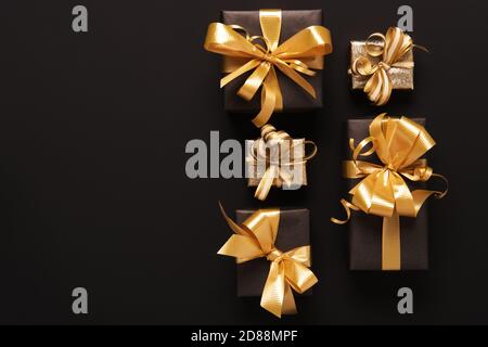 Boîtes-cadeaux dorées emballées de façon festive sur fond noir. Style de pose à plat. Concept des fêtes et du Vendredi fou Banque D'Images