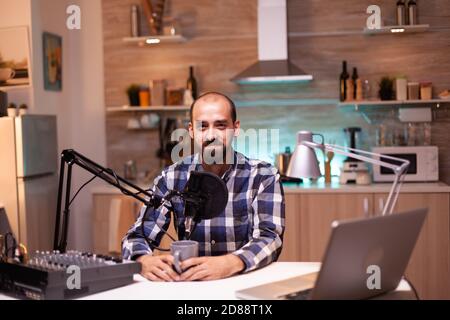 Influenceur tenant une tasse de café et enregistrant un podcast dans un studio à domicile. Production de spectacles en ligne créatifs diffusion Internet diffusion en streaming de contenu en direct, enregistrement de communication numérique sur les réseaux sociaux Banque D'Images