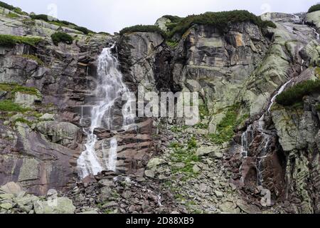 Cascade de montagne à High Tatras (Skok). Grands rochers couverts de gommage. Grande cascade à gauche, petite eau à droite. Banque D'Images