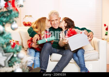 Deux enfants heureux avec des cadeaux embrassent leur grand-père sur le Joue pour Noël Banque D'Images