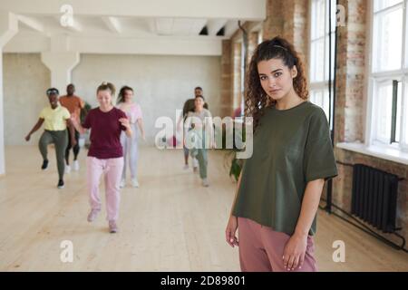 Portrait d'une jeune femme en vêtements de sport regardant l'appareil photo debout dans la salle de sport avec les gens s'entraîner en arrière-plan Banque D'Images