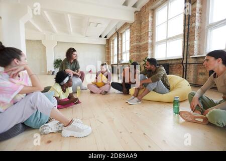 Groupe de jeunes assis sur le plancher discutant de nouveau dansez ensemble en studio de danse Banque D'Images