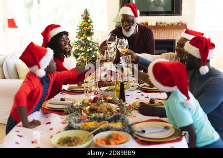 Une famille de plusieurs générations portant des chapeaux de père noël, se portant sur une table à manger dans la salle de séjour à la maison. fête de noël Banque D'Images