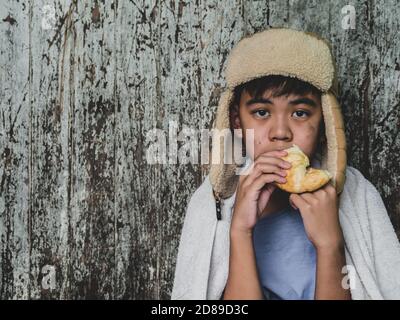 Enfant affamé mangeant du pain qui demande de l'aide pour le don de nourriture de la part des gens dans la rue à la ville. Enfant sans abri non identifié mendiant dans la rue. Elle Banque D'Images