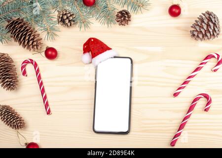 Maquette de smartphone avec décorations de Noël rustiques pour la présentation d'applications. Téléphone portable dans le chapeau du Père Noël. Téléphone noir moderne sur un bureau en bois entouré d'une connexion wi Banque D'Images