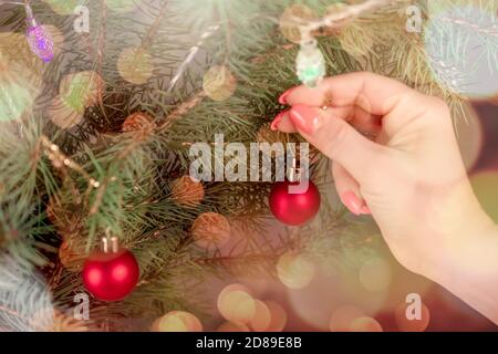 Décoration de l'arbre de Noël. Main de femme est accroché à un ornement boule de Noël sur un arbre de Noël. Arrière-plan de noël flou et lumineux. Banque D'Images