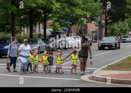 Une ligne de jeunes enfants attachés dans des gilets jaune vif à haute visibilité est escortée en toute sécurité à travers un passage de passage dans une rue de banlieue à Washington, DC Banque D'Images