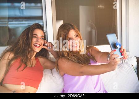 Deux copines prenant Selfie et souriant sur un canapé Banque D'Images