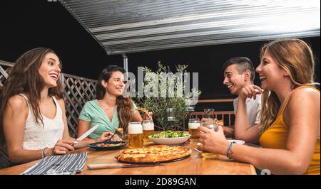 De beaux amis rient et applaudissent avec des bières et manger de la pizza. Groupe de personnes boire et manger concept Banque D'Images