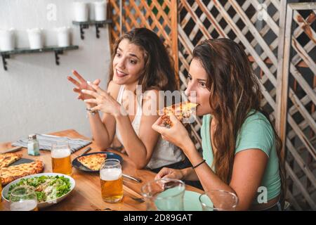 De beaux amis rient et applaudissent avec des bières et manger de la pizza. Groupe de personnes boire et manger concept Banque D'Images