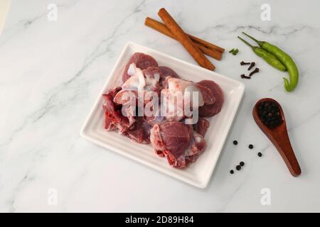 Viande de chèvre ou morceaux de mouton ou d'agneau frais et crus. Préparation du curry de mouton indien. Épice à l'arrière-plan comme des bâtons de cannelle, poudre de piment rouge, Banque D'Images