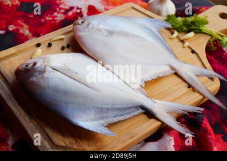 Le poisson blanc de Pomfret est placé sur une planche de bois avec des gousses d'ail, des graines de poivre noir et de la coriandre. Poisson frais de fruits de mer au beurre d'argent. Banque D'Images