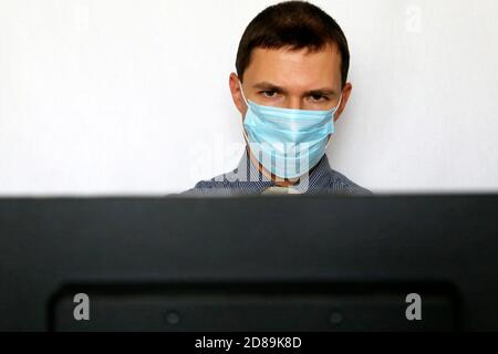 Homme dans le masque de visage assis à l'écran du PC. Sécurité au bureau pendant une pandémie de coronavirus Banque D'Images