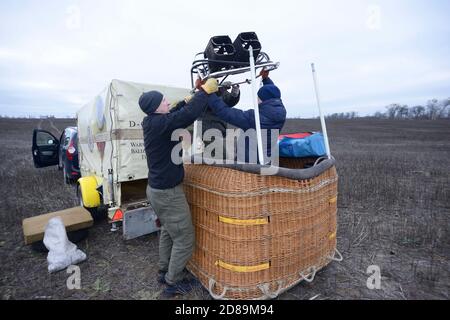 Préparatifs pour le vol en montgolfière : les hommes plaçant le brûleur à gaz sur le dessus du panier, de la voiture et de la remorque avec l'équipement installé sur un arrière-plan Banque D'Images