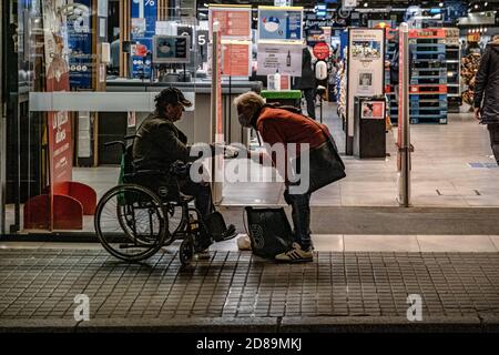 Barcelone, Espagne. 27 octobre 2020. On voit une femme donner de la nourriture à un homme handicapé dans un fauteuil roulant qui demande des almes à la porte du supermarché Carrefour sur la Rambla à Barcelone. La situation pandémique s'aggrave à Barcelone en raison de l'augmentation des cas d'infections à Covid19. Barcelone devra faire face à de nouvelles mesures restrictives pour la mobilité des citoyens à partir de cette semaine. La réduction des heures d'ouverture fait avancer la fermeture à 9 h 00 et une heure plus tard le début du couvre-feu pour tous les citoyens qui n'ont pas de preuve de mobilité autorisée. Crédit : SOPA Images Limited/Alamy Live News Banque D'Images