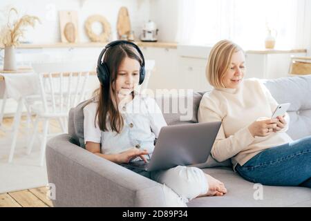 Maman et fille sont assis sur le canapé et surfent dans des gadgets. Banque D'Images