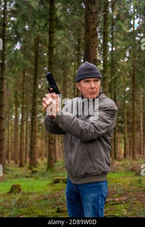 Homme tenant un pistolet, fond de forêt Banque D'Images