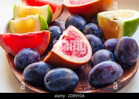 Des tranches de pamplemousse et de prunes sur une assiette en bois, gros plan. Fond de fruits frais d'été Banque D'Images
