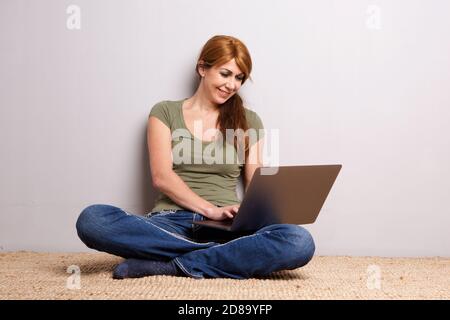 Portrait d'une femme mûre attrayante assise sur le sol à la maison et travailler sur un ordinateur portable Banque D'Images