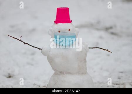 Bonhomme de neige portant un masque de protection debout à l'extérieur sur une aire de jeux lors d'une journée hivernale enneigée. Concept de protection Covis. Nouvelle normale Banque D'Images