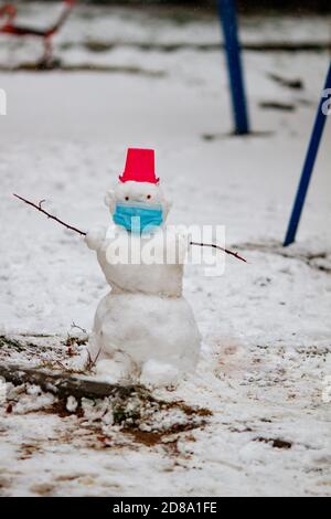 Bonhomme de neige portant un masque de protection debout à l'extérieur sur une aire de jeux lors d'une journée hivernale enneigée. Concept de protection Covis. Nouvelle normale Banque D'Images