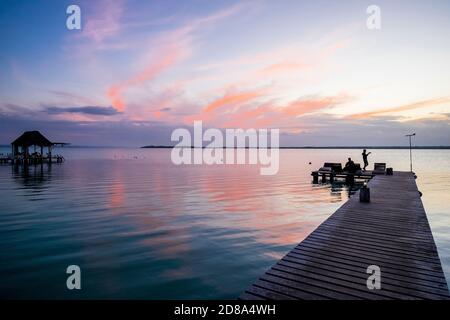 Bacalar, Yucatan, Mexique - 11 mars 2020 : un couple sur une jetée sur la lagune de Bacalar, Mexique prêt à enregistrer la montée du soleil à l'aube. Banque D'Images