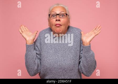 Perplexe, la femme âgée regarde dans la confusion, hausse les épaules comme ne sait pas la réponse, étant infondée et incertaine Banque D'Images