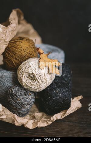 Balles de fil confortables pour tricoter à la main avec une feuille de chêne sèche sur un fond sombre. Fond d'automne pour la maison artisanale et lente. Mise au point sélective. Banque D'Images