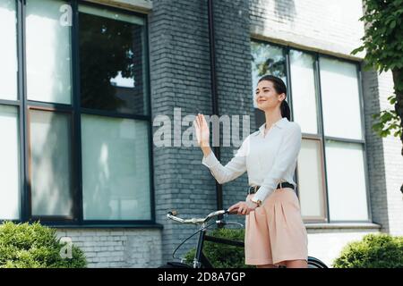 jeune femme d'affaires gaie debout avec le vélo et la main de la main de la main Banque D'Images