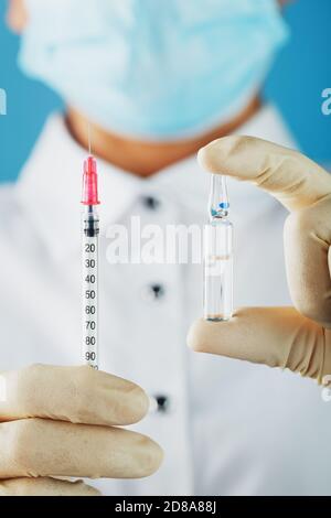 Le médecin tient avec des gants de protection et un masque tient l'ampoule avec le vaccin. Banque D'Images