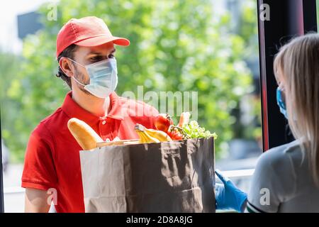 Objectif sélectif du service de messagerie donnant le sac en papier avec l'épicerie à femme en masque médical Banque D'Images