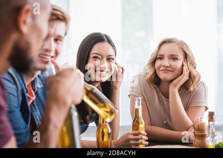 concentration sélective d'amis multiculturels joyeux avec des bouteilles de bière parler pendant la fête Banque D'Images