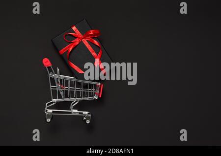 Concept de solde du Vendredi fou. Cadeau noir avec ruban rouge dans le panier sur fond sombre. Shopping de vacances pour des cadeaux de Noël, Saint Valentin Banque D'Images