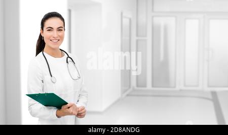 Portrait souriant médecin avec stéthoscope autour de son cou regardant la caméra et debout à l'hôpital moderne Banque D'Images