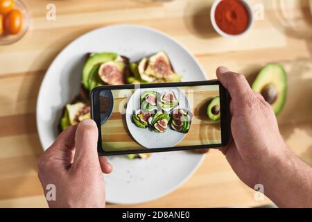 Gros plan de l'homme tenant un téléphone mobile et faisant la photo de sandwiches sur l'assiette avec des légumes frais Banque D'Images