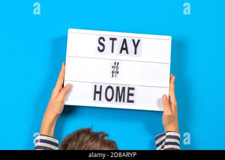 Les mains des enfants tiennent une visionneuse blanche avec texte RESTENT À LA MAISON sur fond bleu. Coronavirus, Covid-19, quarantaines et concept de distanciation sociale Banque D'Images