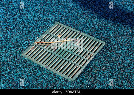 Vue sur la vidange d'eau sur le terrain de jeu du parc aquatique qui tourne bleu en raison de la mauvaise qualité du couvercle en caoutchouc fait à partir de Granulés EPDM vierges fins Banque D'Images