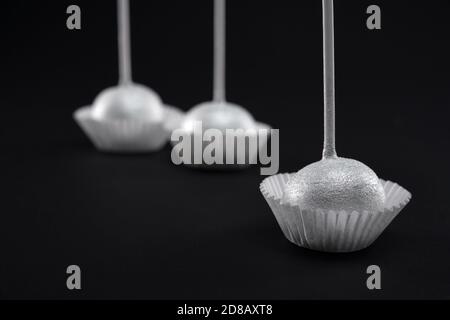 Gros plan de trois gâteaux glacés en argent doux sur de longs bâtonnets dans des paniers en papier blanc. Délicieux bonbons frais isolés sur fond noir. Concept de desserts, confiserie. Banque D'Images