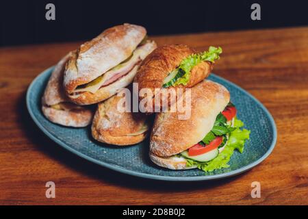 Assortiment de délicieux sandwichs à base de baguette, remplis de jambon en tranches fines ou salami et laitue verte fraîche ou basilic disposés dans un ligne oblique sur un ancien Banque D'Images